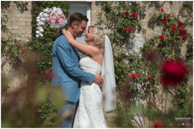 Bride and groom photographed through red roses at front of Smeetham hall