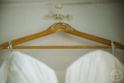 Photo of a personalised wooden wedding hanger with floral hand-painted details for a bride, used in elegant wedding photography in Essex and Suffolk. Delicate wooden wedding hanger with the name "Ginev" handwritten and floral decorations, hanging in a bridal wardrobe for Essex and Suffolk wedding photography.