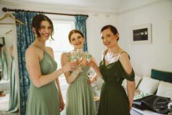 Joyful bridesmaids celebrating with champagne before the wedding in a charming, well-lit room with elegant décor in Essex & Suffolk. Elegant bridal party toasting with champagne in a beautifully decorated bedroom at a wedding in Essex & Suffolk. Bright natural light and stylish attire create a joyful atmosphere.