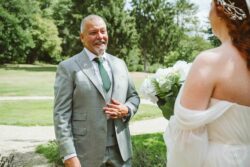 A bride and her father share an emotional moment during a wedding ceremony in a scenic outdoor location with lush greenery and bright natural light. Emotionally touching moment of a bride and her father sharing a heartfelt wedding moment outdoors, with lush green trees and bright sunlight creating a beautiful setting.