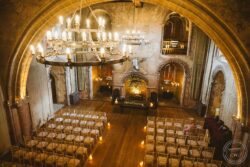 Charming wedding ceremony space in a historic Essex chapel, featuring warm candlelight, ornate stone features, and a stunning chandelier, ideal for memorable wedding events in Suffolk. Vintage stone chapel interior with grand chandelier, candlelit ceremony setup, wooden chairs, and elegant gothic architecture, perfect for weddings in Essex & Suffolk.