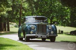 A beautiful vintage Rolls-Royce wedding car decorated with ribbon, set in a picturesque outdoor setting for a wedding in Essex & Suffolk. Classic vintage Rolls-Royce parked on a lush green lawn during a wedding in Essex & Suffolk, captured by Lavenham Photographic.