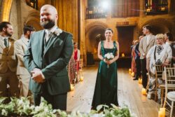 A joyful bride in a green dress holding a white bouquet stands amidst guests during a wedding celebration. Elegant wedding ceremony inside historic venue with romantic candlelit ambiance and beautifully dressed guests in formal attire.