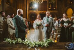 A joyful bride in a flowing white gown holding a bouquet, walking arm-in-arm with her proud father during a wedding service. Elegant wedding ceremony inside a historic church with a happy bride walking down the aisle surrounded by family and friends.
