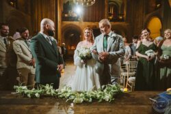 A heartfelt wedding moment with the bride and groom standing before the officiant, exchanging vows in a decorated historic church in Essex, with bridal party and guests witnessing the ceremony. Elegant wedding ceremony inside a historic church in Essex, featuring the bride and groom exchanging vows surrounded by bridesmaids and groomsmen, with warm, ambient lighting and floral arrangements.