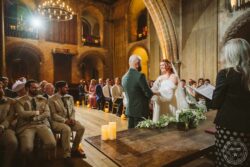A joyful moment during a wedding ceremony at a historic Essex church, featuring a smiling bride and groom exchanging vows, with family and friends witnessing in a beautifully lit, stone-arched venue. Elegant wedding ceremony in historic Essex church with redheaded bride and groom exchanging vows, surrounded by joyful guests and atmospheric candlelight.
