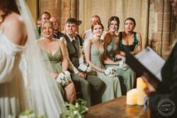 Wedding ceremony with bridesmaids in sage green dresses and white bouquets, seated attentively in a rustic venue with candlelit decor, showcasing a joyful and emotional atmosphere. Elegant bridesmaids seated during a wedding ceremony in a historic venue, holding white floral bouquets, with warm ambient lighting and exposed brick walls, capturing a heartfelt moment.